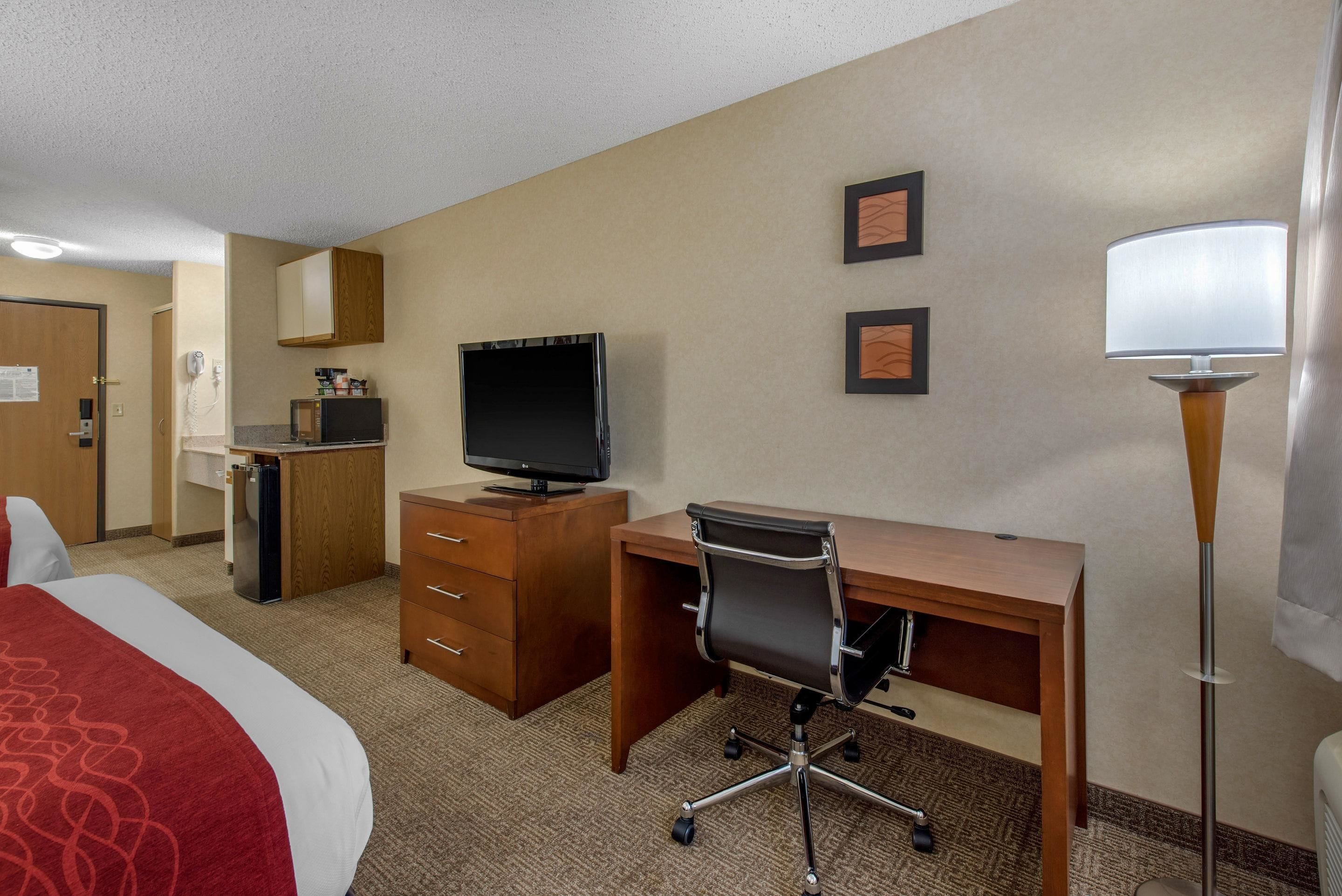 A hotel room with a bed, desk, chair, television, minibar, and a lamp.