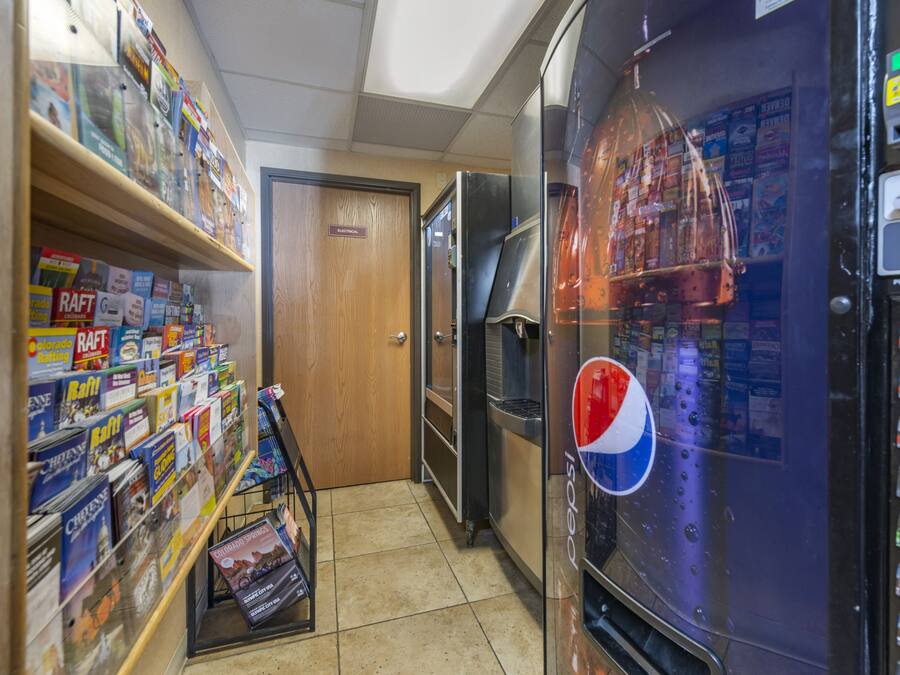 Un pasillo estrecho con una máquina expendedora, un refrigerador y estantes llenos de revistas.