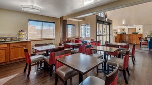 Un espace de restauration d’hôtel comprenant plusieurs tables et chaises, un plancher en bois et de grandes fenêtres laissant entrer la lumière naturelle.