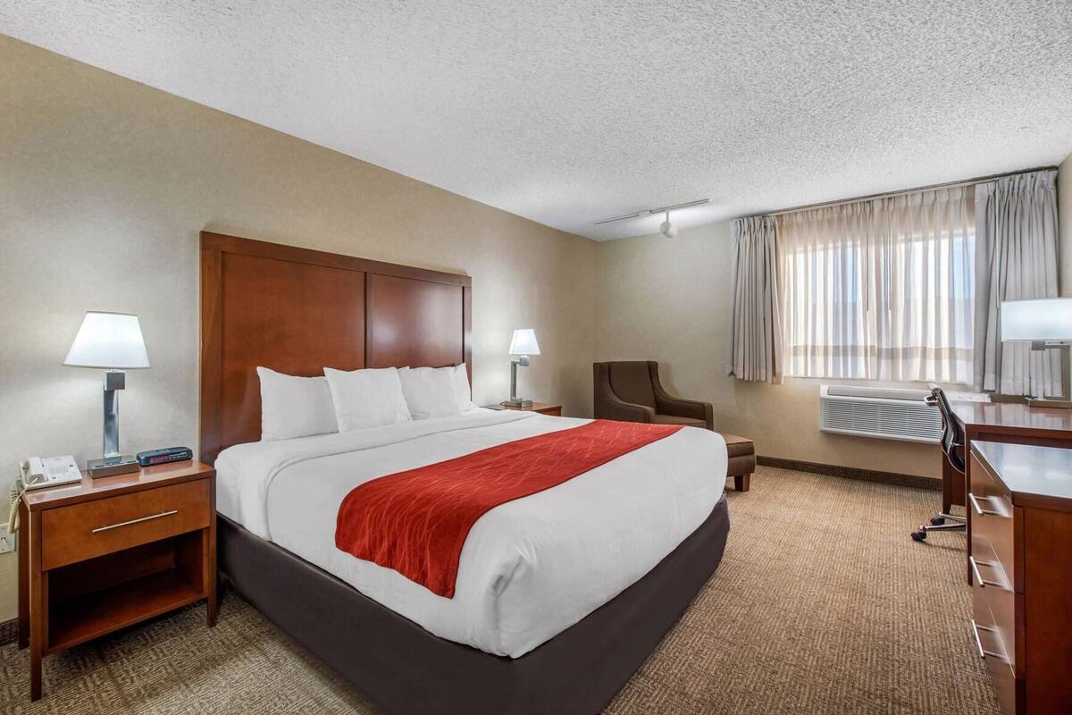 A hotel room with a large bed, two bedside tables, a desk, a chair, and a window with curtains.