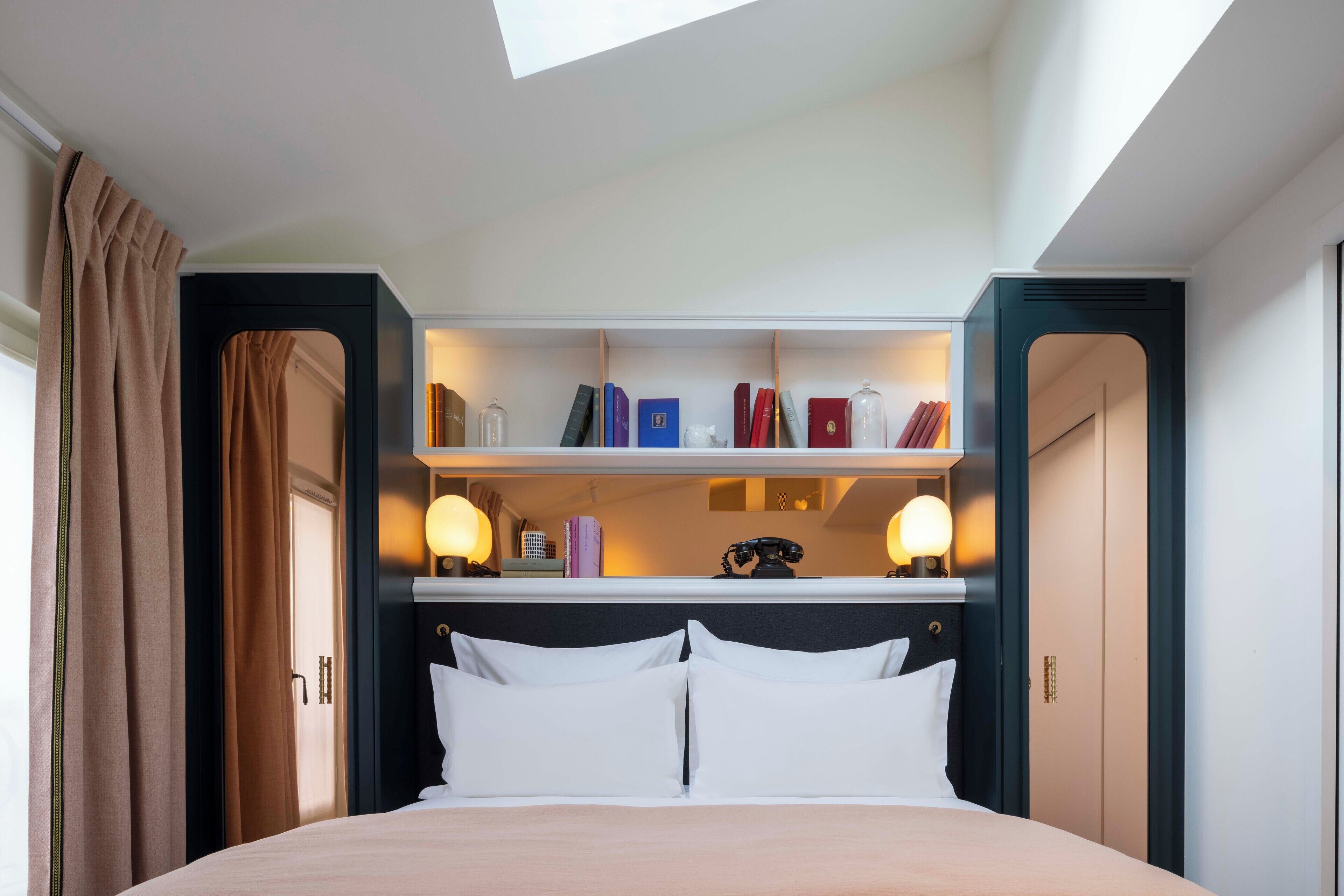 A hotel room with a bed, a built-in bookshelf, and a skylight.