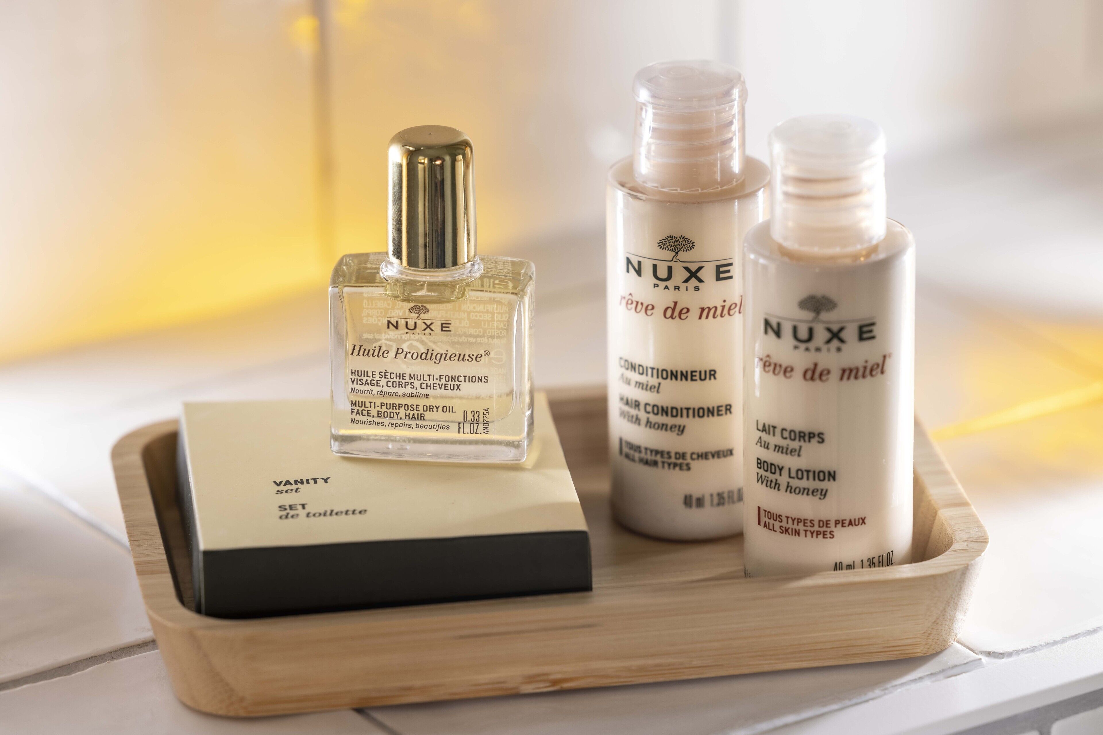 A wooden tray with three Nuxe Paris products: a set of toiletries, a hair conditioner, and a body lotion.