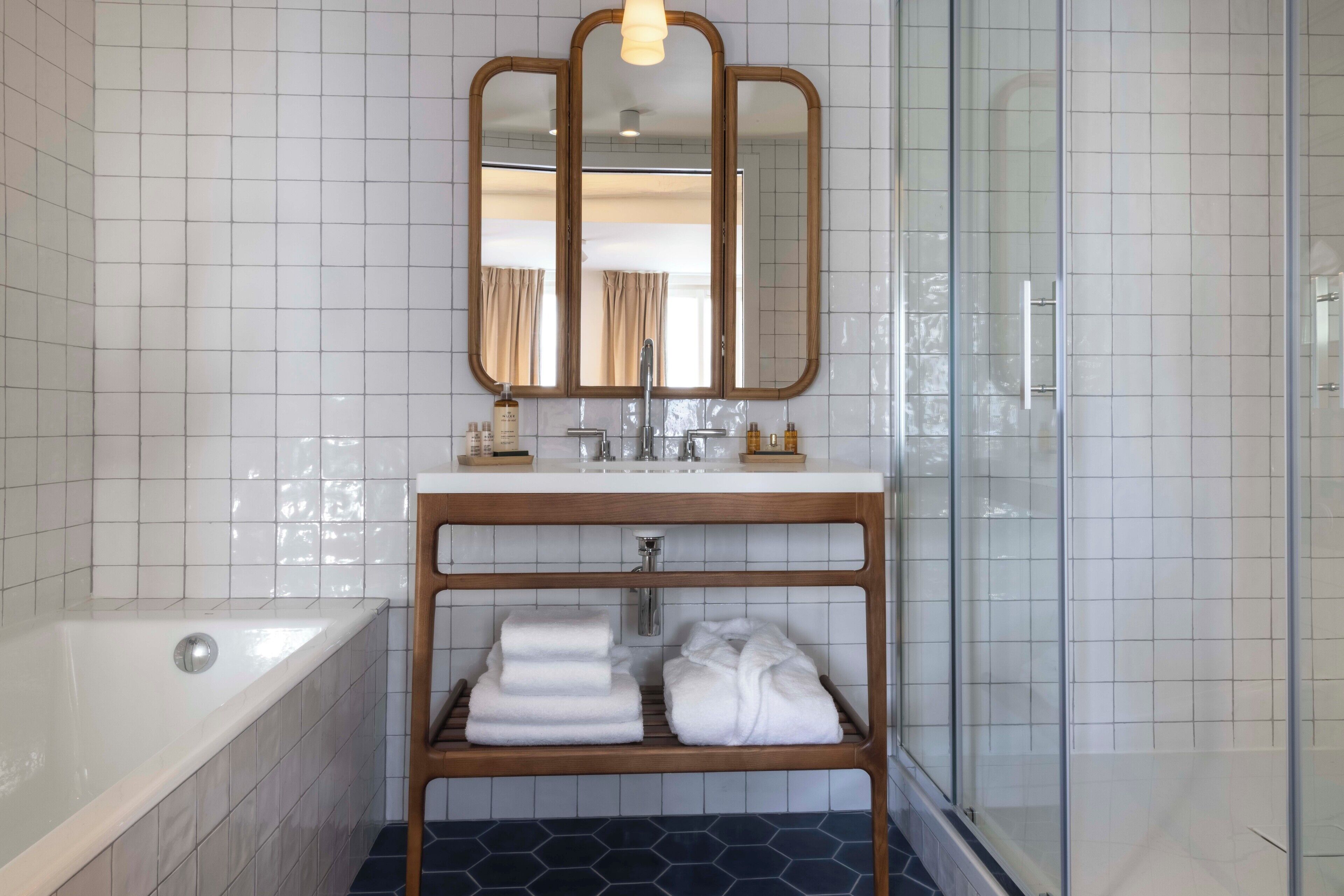 A modern bathroom with a white tiled wall, a wooden vanity, a large mirror, a bathtub, and a shower area.