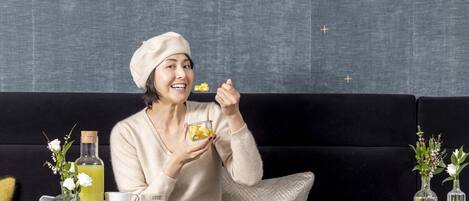 A person sitting on a black sofa with a tray of food and drinks in front of them.