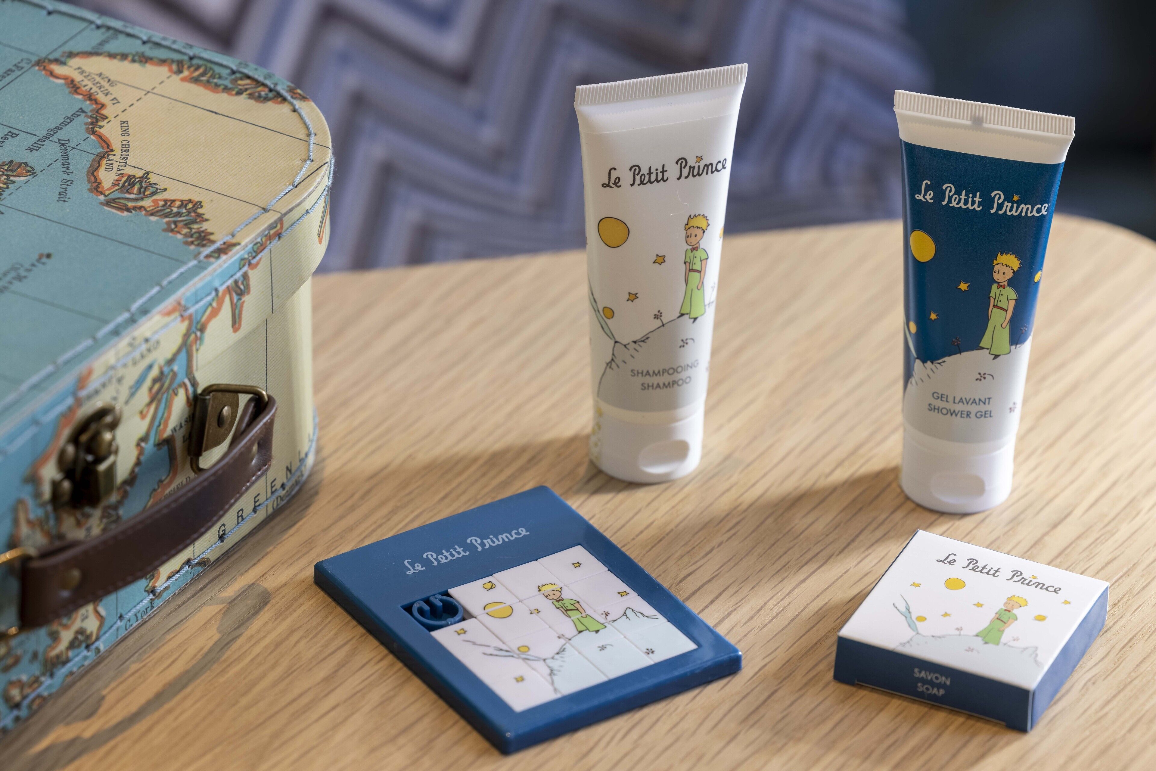 A wooden table with a vintage map, two tubes of Le Petit Prince shampoo, and two boxes of Le Petit Prince soap.