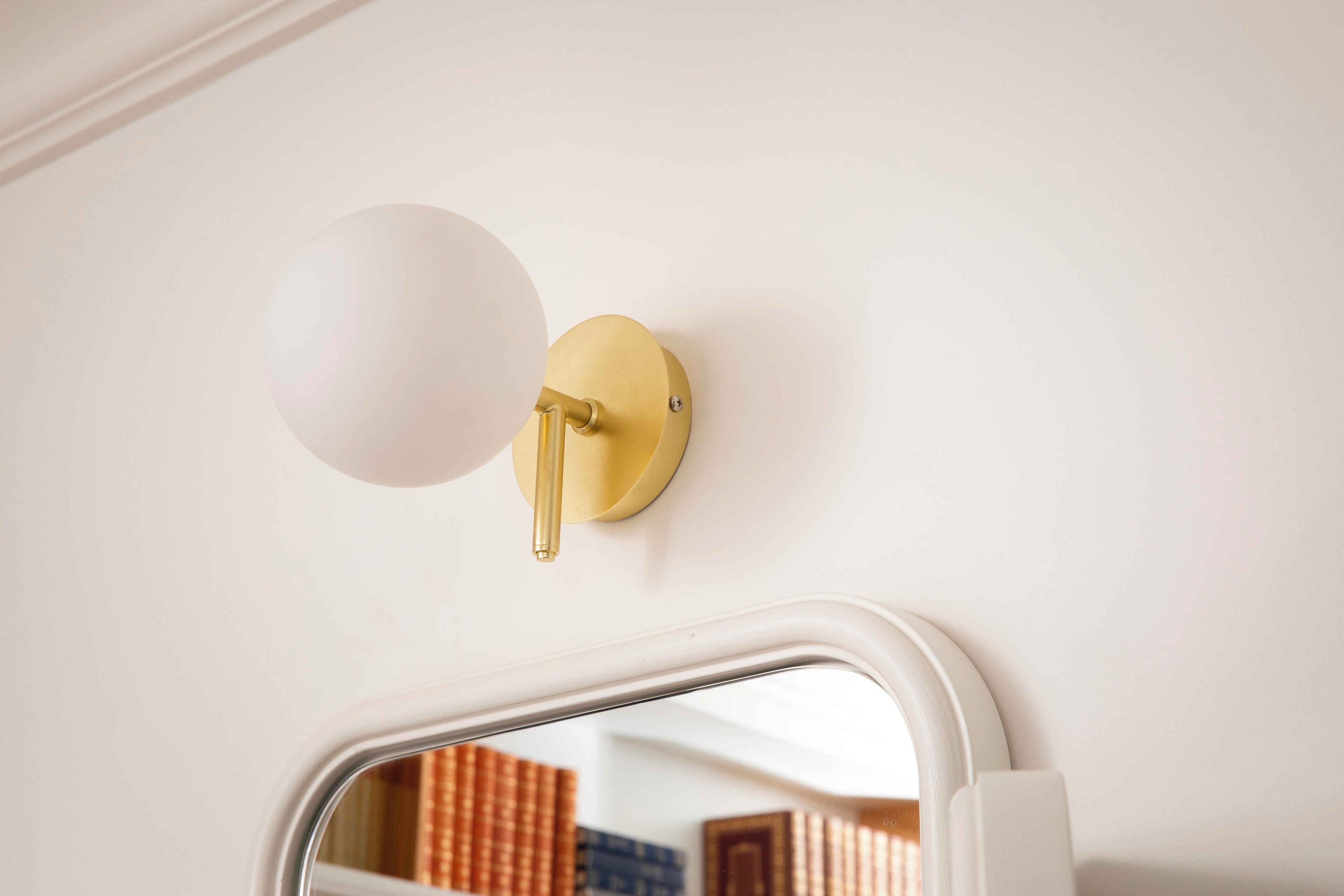 A wall-mounted light fixture with a spherical shade and a brass pull chain.