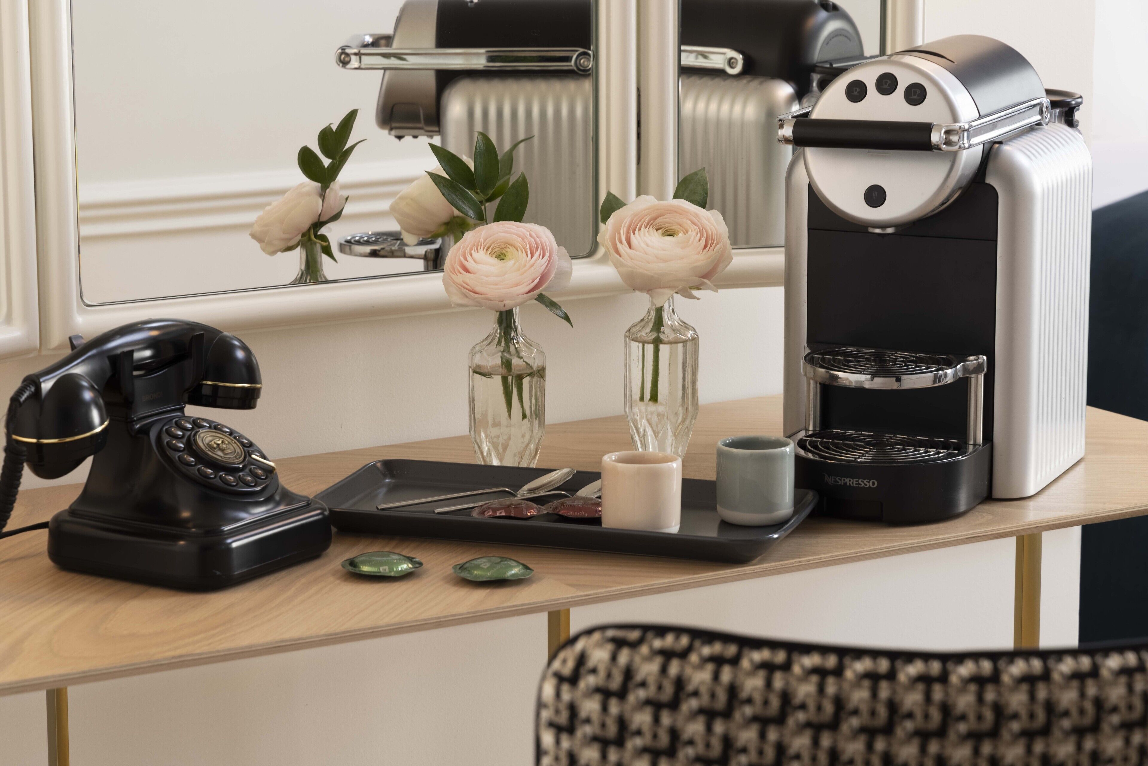A coffee machine, a telephone, and two vases with flowers on a wooden table.
