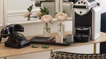 A coffee machine, a telephone, and two vases with flowers on a wooden table.