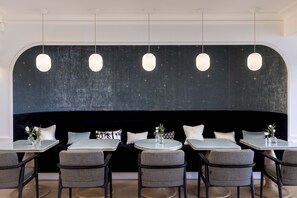 Un restaurant avec des tables rondes, des chaises grises et des lampes suspendues.