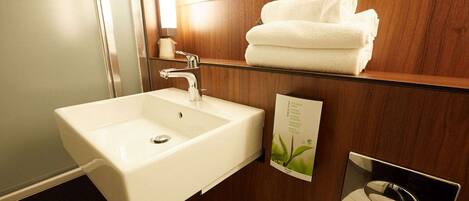 A bathroom with a white sink, a mirror, and a shelf with folded towels.