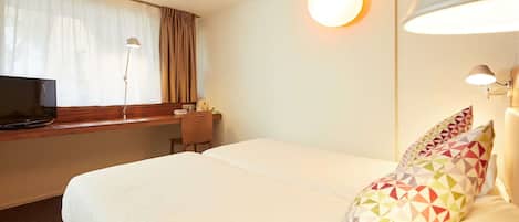 Habitación de hotel con cama, escritorio, televisor y lámpara.