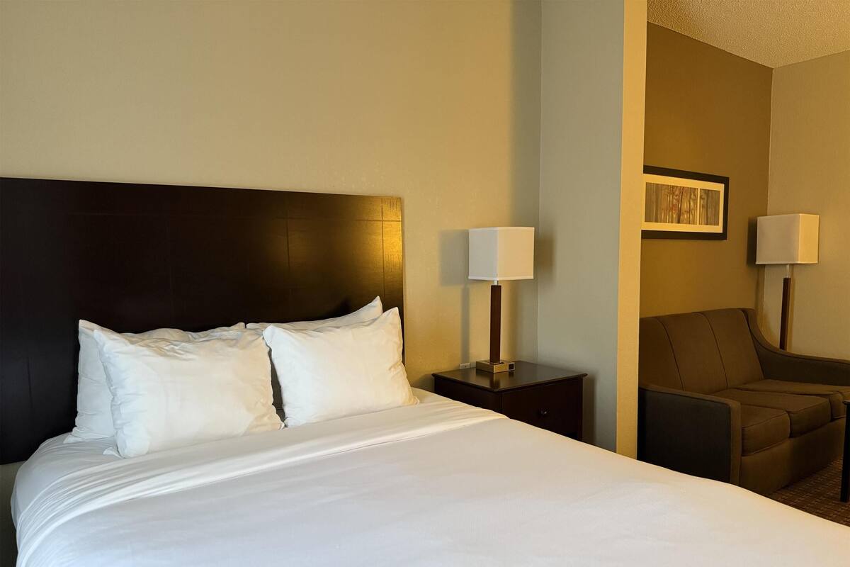 A hotel room with a large bed, two bedside lamps, a chair, and a painting on the wall.
