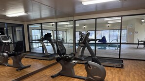 Et fitnessrum med træningsudstyr, store vinduer og trægulv.