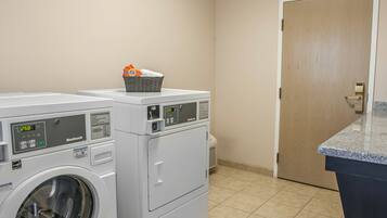 A laundry room with two front-loading washing machines, a basket on the top of one, and a door in the background.