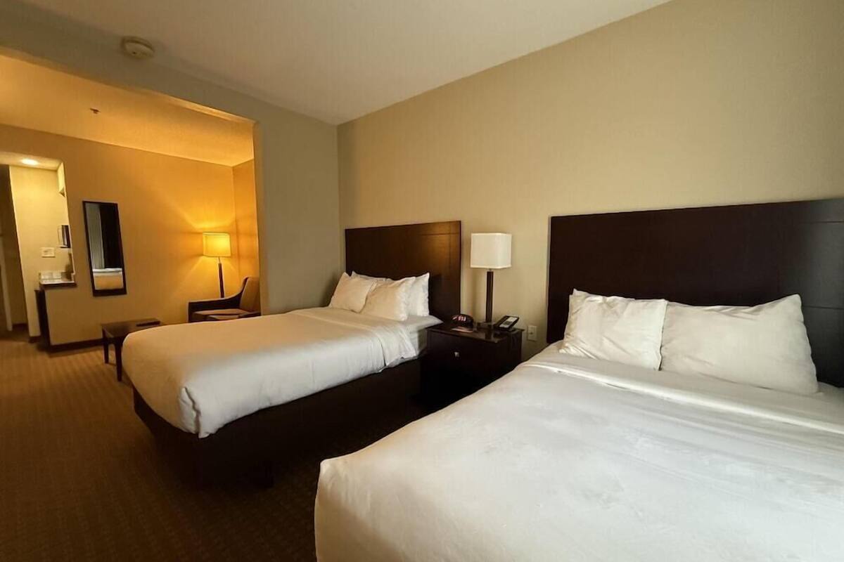 A hotel room with two beds, a nightstand with a lamp, a chair, and a mirror on the wall.