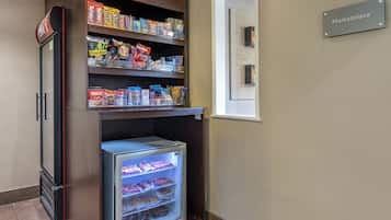 A kitchenette with a refrigerator, shelves stocked with snacks, and a sign indicating a marketplace.
