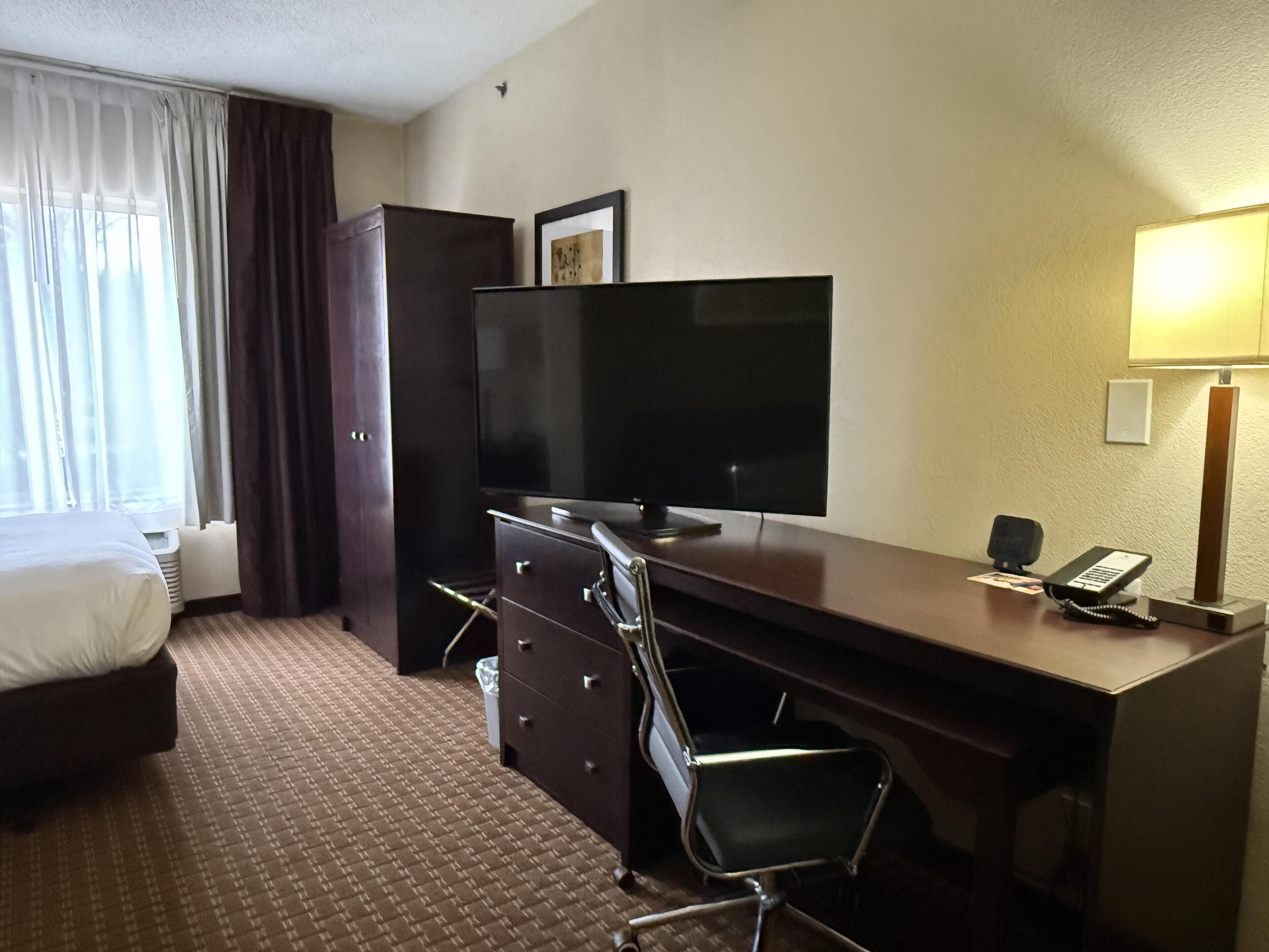 Habitación de hotel con cama, escritorio, televisor de pantalla plana, silla, lámpara y teléfono.