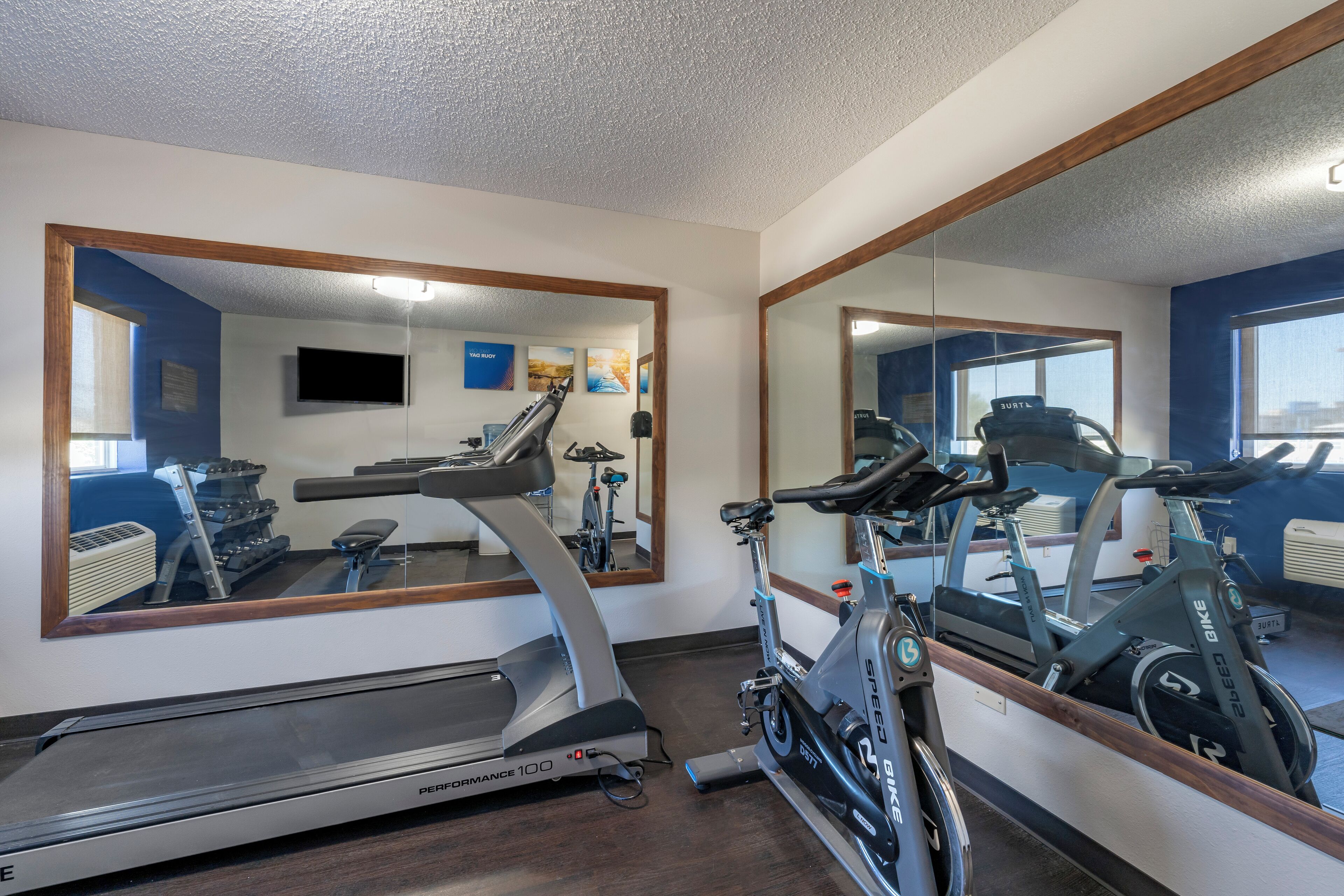 A gym with a treadmill, stationary bikes, and a mirror reflecting the equipment.