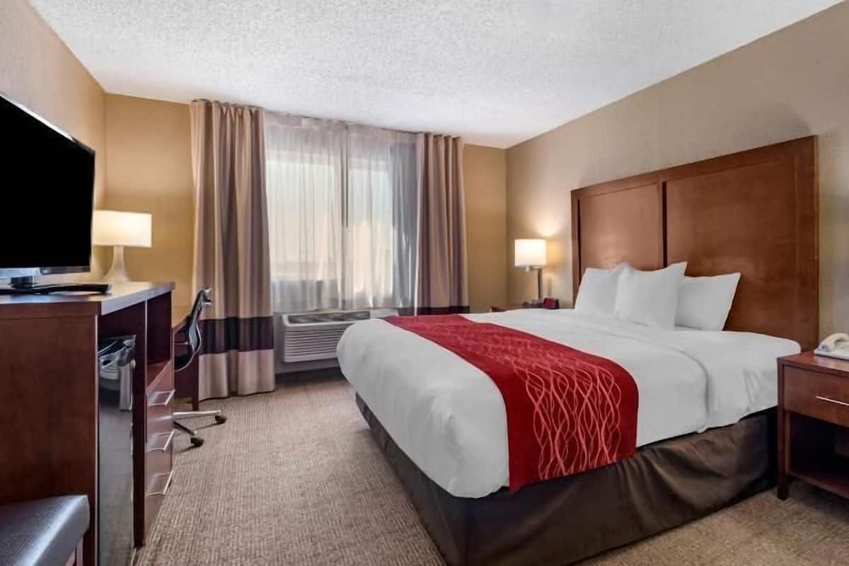 A hotel room with a bed, bedside tables, a desk, a TV, and a window with curtains.