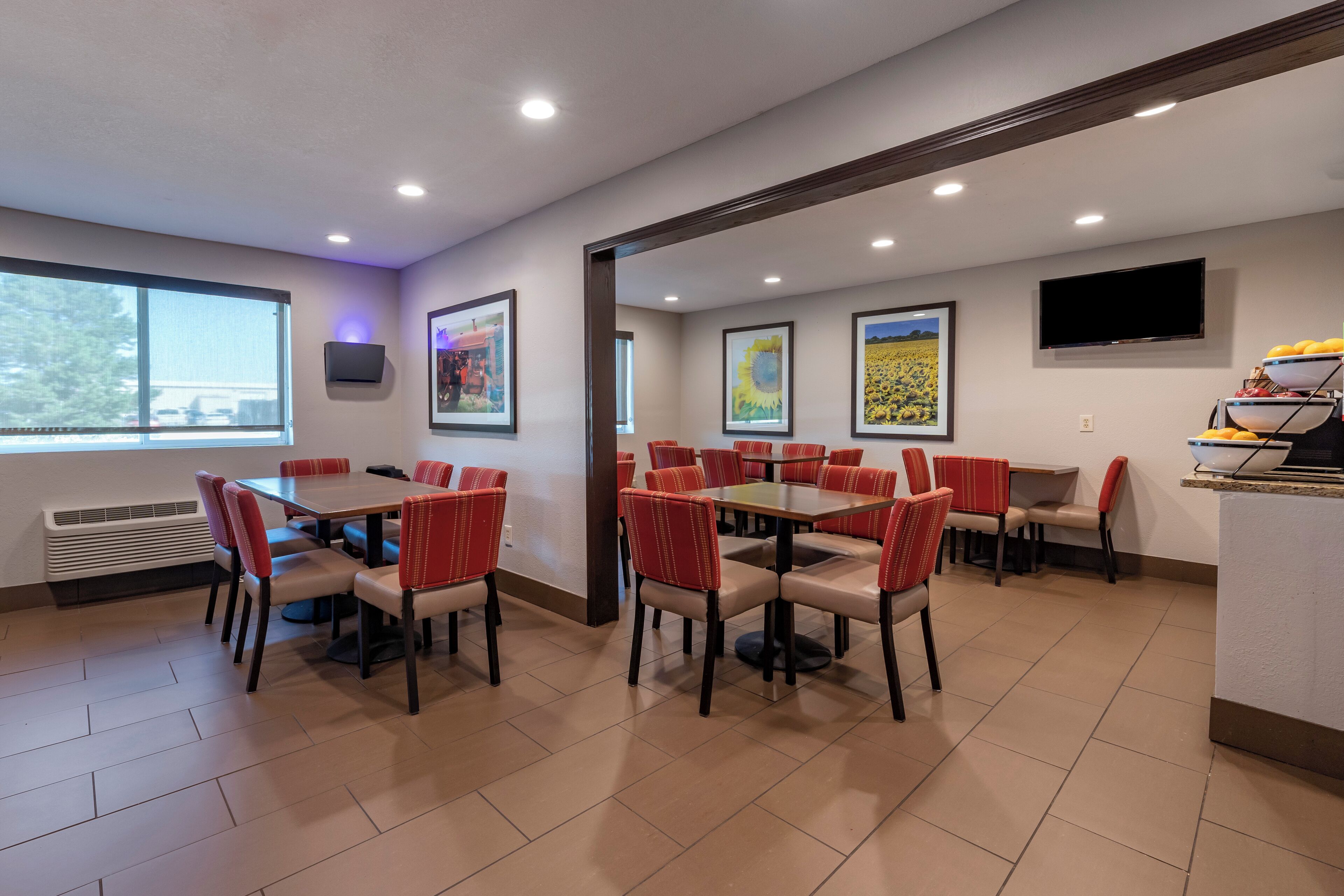 A dining area with multiple tables and chairs, a flat-screen TV mounted on the wall, and framed artwork on the walls.