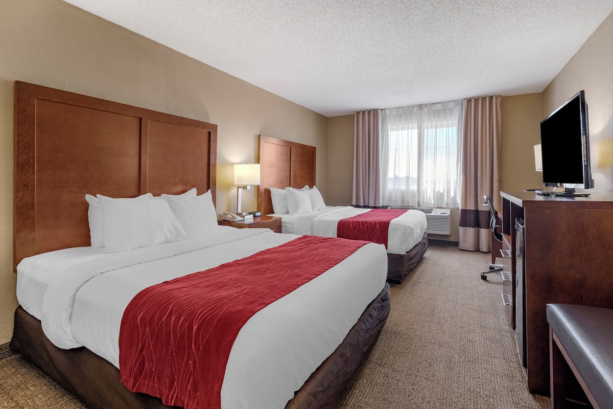 A hotel room with two beds, a TV, a desk, and a window with curtains.