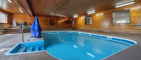 An indoor swimming pool with a wooden interior, a blue pool edge, and a ladder leading into the water.