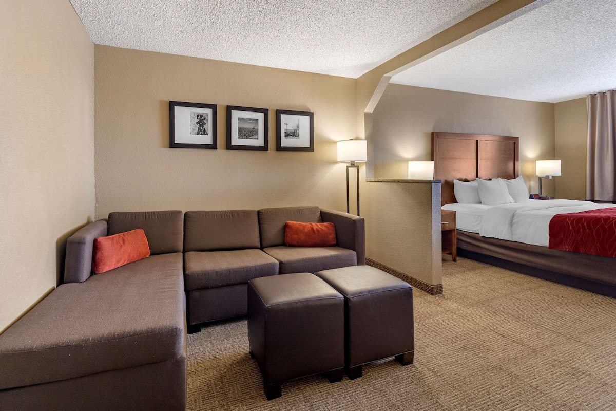 A hotel room with a sectional sofa, a bed, a nightstand, and framed pictures on the wall.