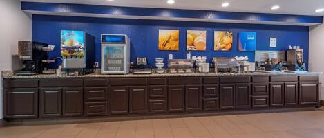 A breakfast bar with a coffee machine, juice dispenser, and various food items.