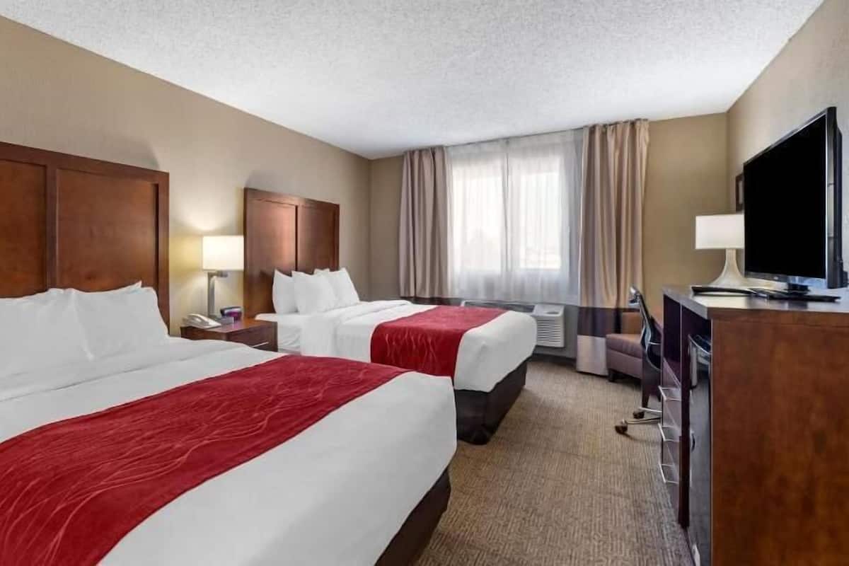A hotel room with two beds, a desk, a TV, and a window with curtains.