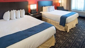 A hotel room with two beds, a red accent wall, framed artwork, a nightstand with a lamp, and a patterned carpet. - Quality Inn Brooklyn Center (Brooklyn Center)