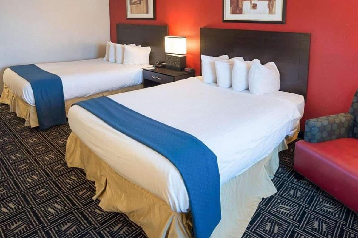 A hotel room with two beds, a red wall, and a patterned carpet.