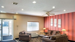 A hotel room with two sofas, a coffee table, a standing lamp, a ceiling fan, and a large window with blinds. - Quality Inn Brooklyn Center (Brooklyn Center)