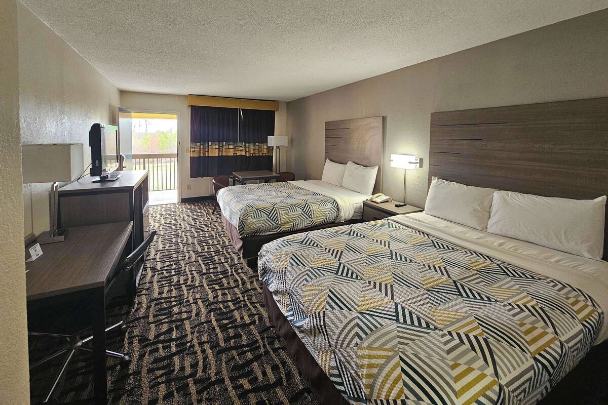 A hotel room with two beds, a desk, a chair, a TV, and a balcony with curtains.