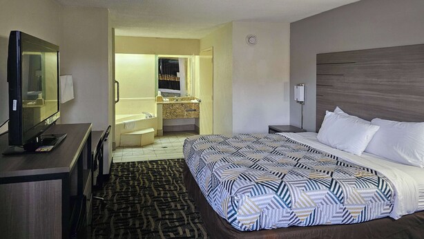 Ein Hotelzimmer mit Bett, Schreibtisch, Fernseher, Badezimmer mit Waschbecken und Spiegel sowie Teppichboden.