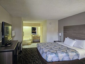 Une chambre d’hôtel comprenant un lit, un bureau, une télévision, une salle de bain avec un lavabo et un miroir, et un sol recouvert de moquette.