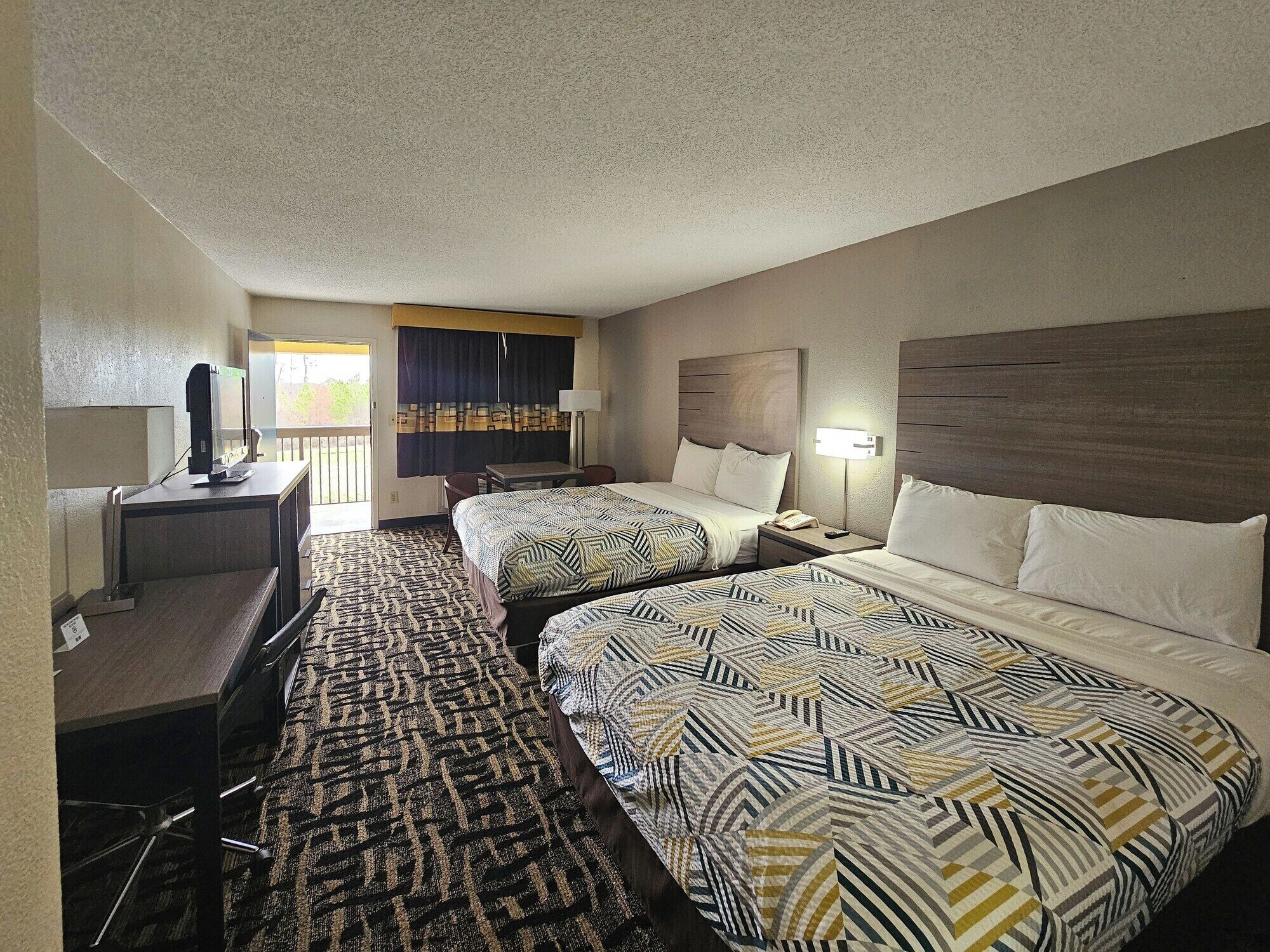 A hotel room with two beds, a desk, a chair, a TV, and a balcony with curtains.