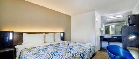 Quarto de hotel com cama, mesa de cabeceira e uma cadeira azul.