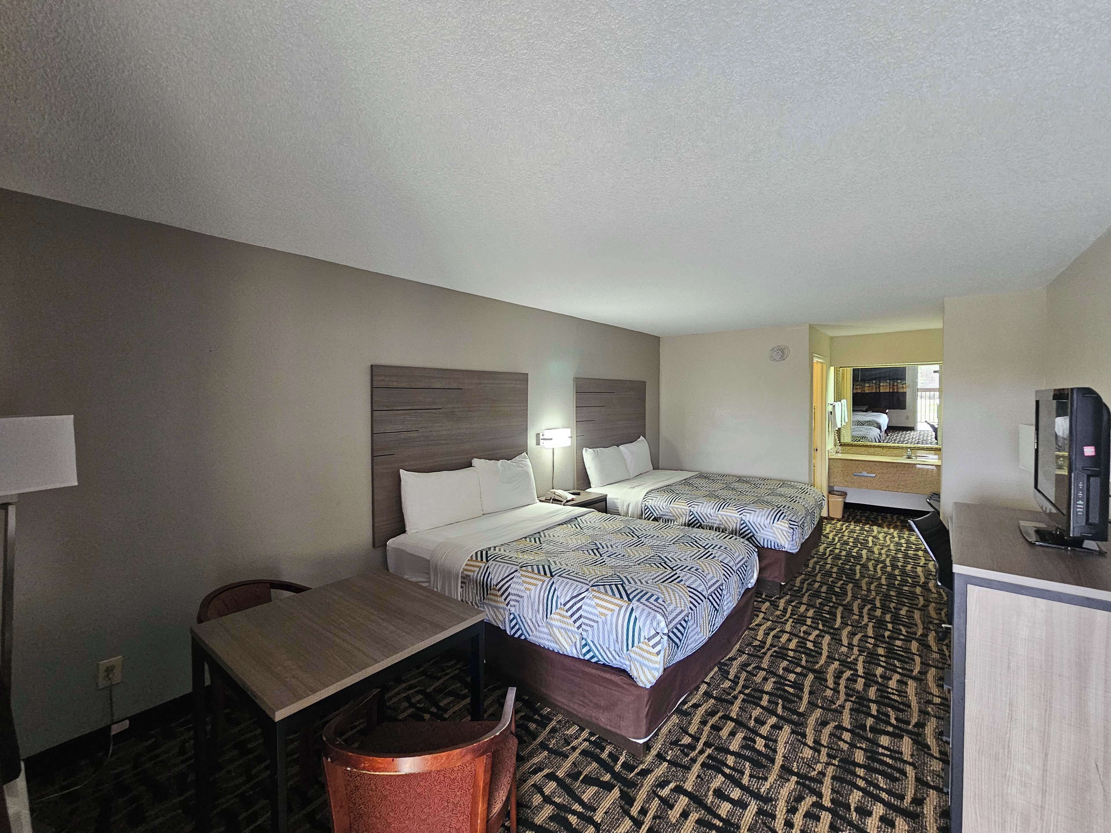 A hotel room with two beds, a desk, a chair, a television, and a bathroom visible through an open door.
