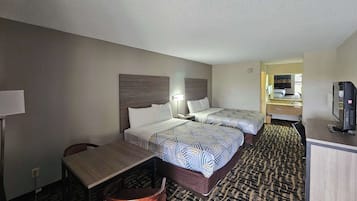 A hotel room with two beds, a desk, a chair, a television, and a bathroom visible through an open door.