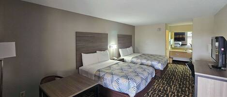 Habitación de hotel con dos camas, un escritorio, una silla, un televisor y un baño visible a través de una puerta abierta.