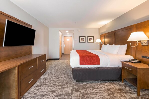 A hotel room with a large bed, a flat-screen TV, wooden furniture, and two wall-mounted lamps.