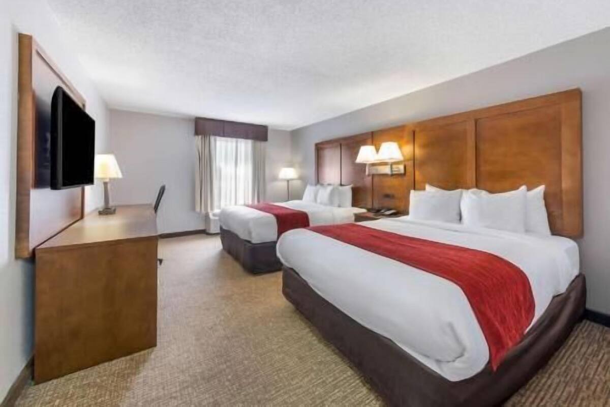 A hotel room with two beds, a desk, a TV, and a large wooden headboard.