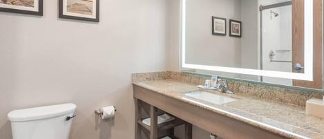A bathroom with a toilet, sink, and mirror. There are two framed pictures on the wall.