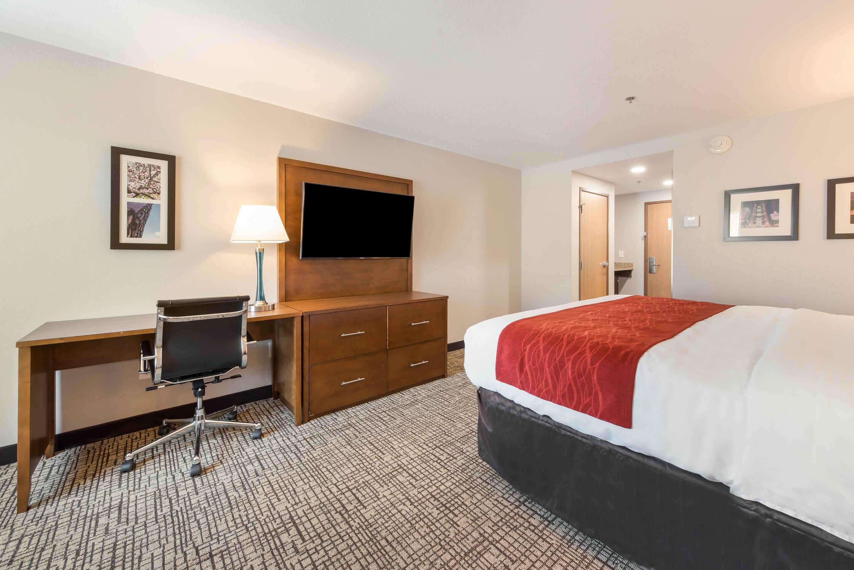 Quarto de hotel com cama, escrivaninha, cadeira, televisão e cómoda.