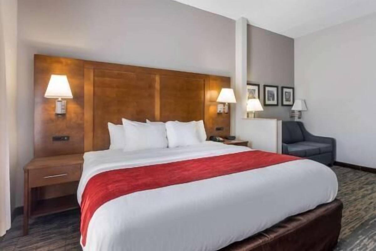 Une chambre d’hôtel avec un grand lit, deux tables de chevet, un bureau avec une chaise et des lampes fixées au mur.