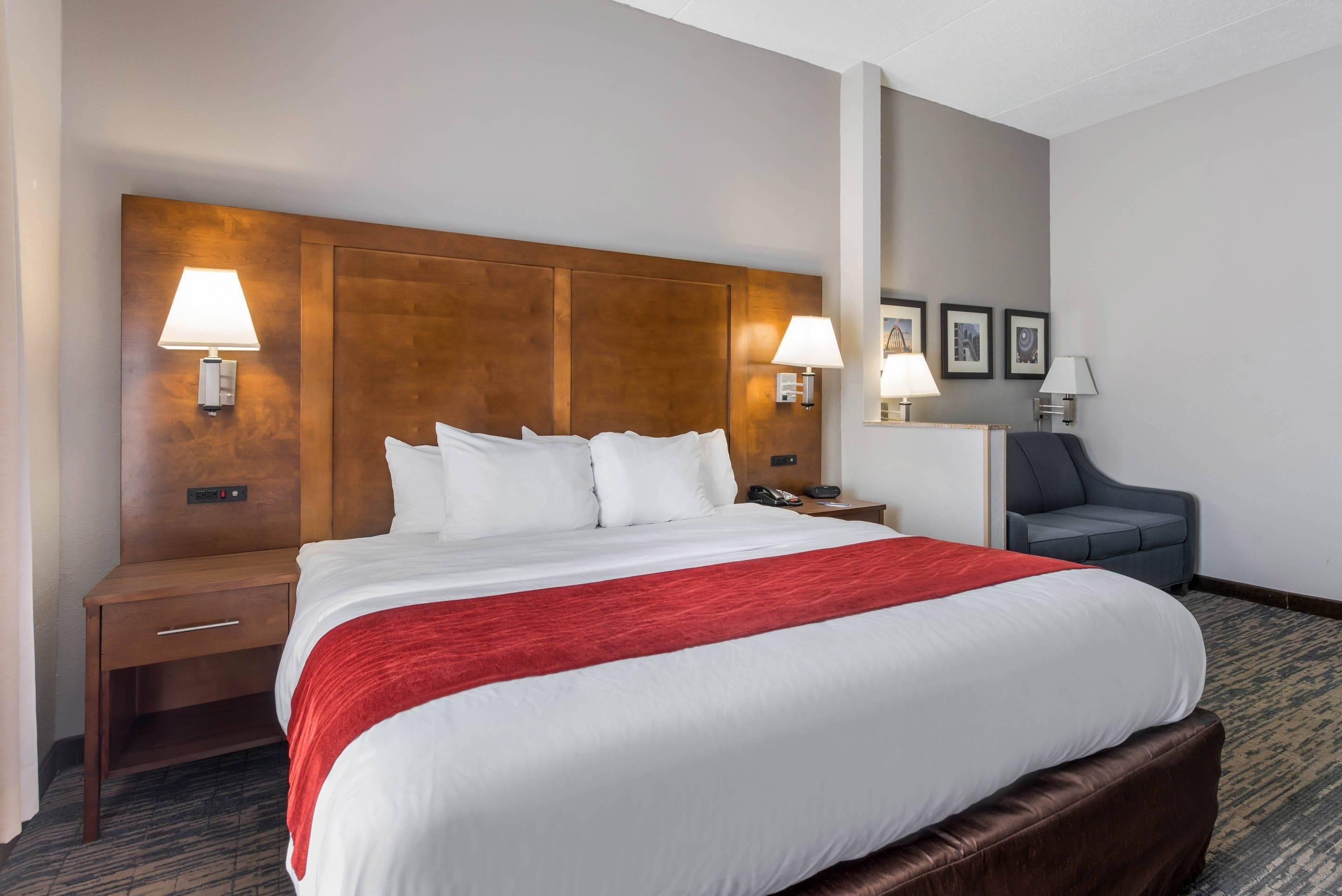A hotel room with a large bed, two bedside lamps, a nightstand, a chair, and framed pictures on the wall.
