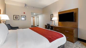 A hotel room with a large bed, a desk, a chair, a TV mounted on the wall, and a lamp.