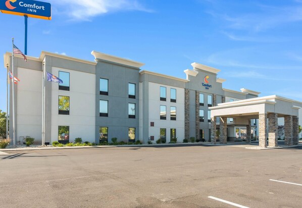 A Comfort Inn hotel with a modern design, featuring a spacious parking lot and a clear blue sky.
