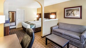 Une chambre d’hôtel avec un lit, un canapé, une table et une chaise. Une porte donne accès à une autre pièce.
