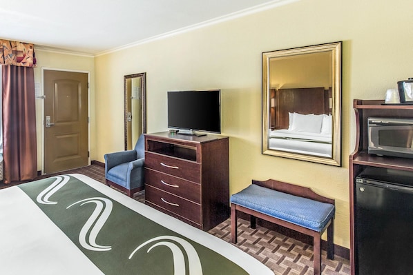 A hotel room with a bed, a TV, a dresser, a bench, a mirror, and a microwave.
